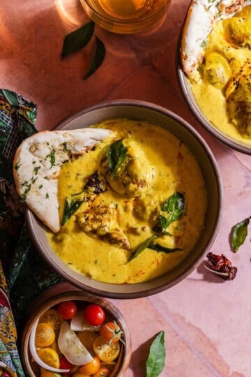 Two bowls of curry with bread and vegetables.