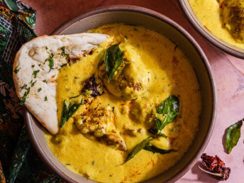 Two bowls of curry with bread and vegetables.