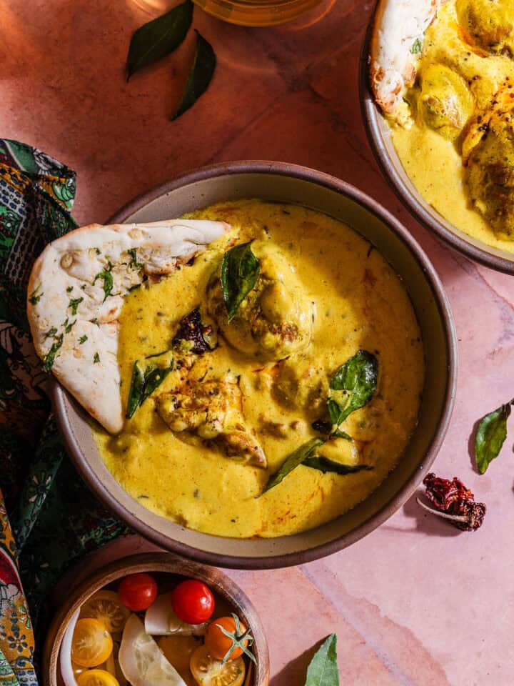 Two bowls of curry with bread and vegetables.