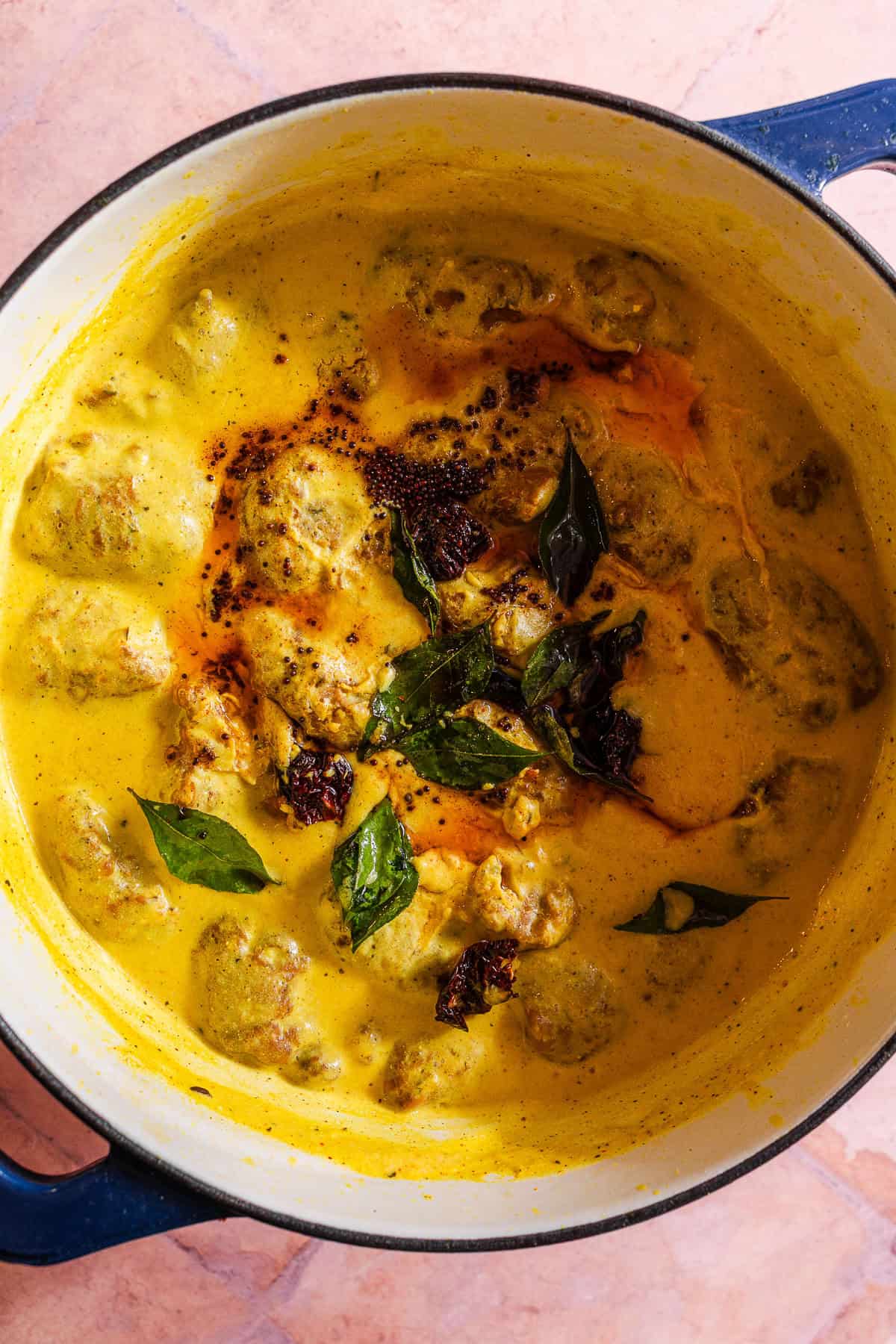 A dutch oven full of kadhi topped with a tadka of spices and curry leaves.