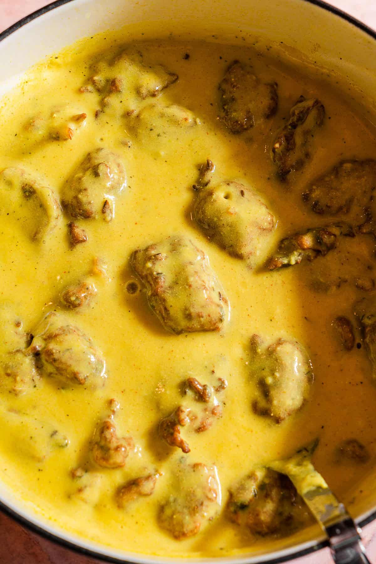 A dutch oven filled with yellow kadhi and pakoras.