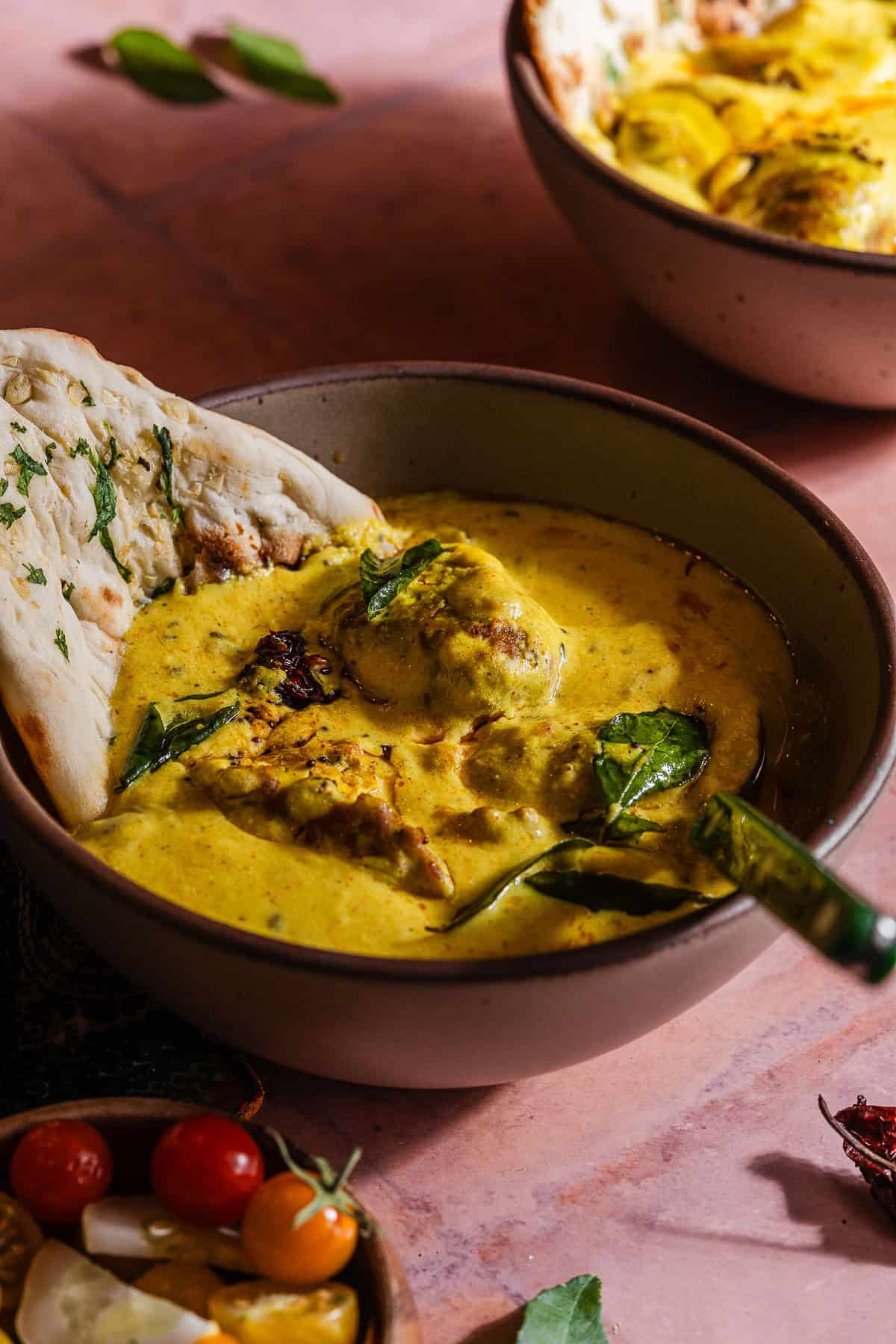 Two bowls of curry with bread and vegetables.