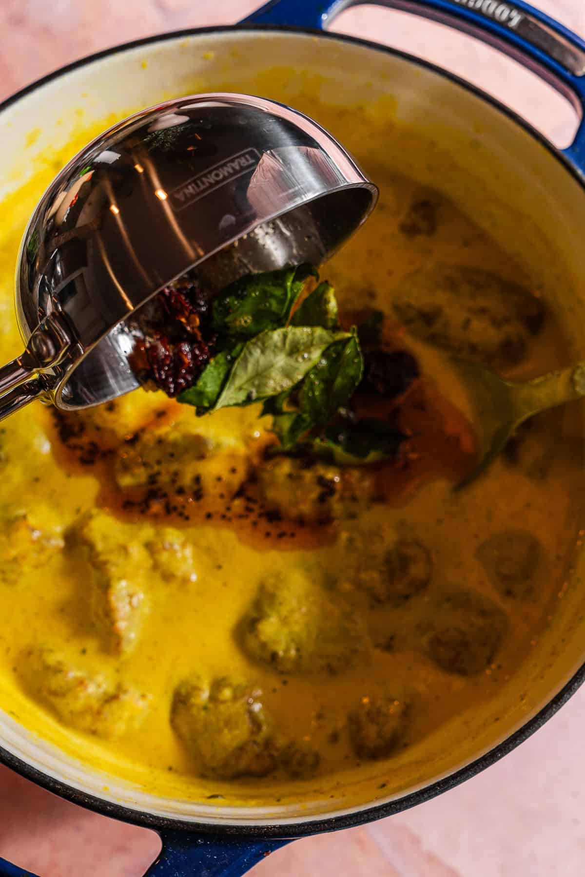 Pouring a tadka of curry leaves and spices over kadhi.