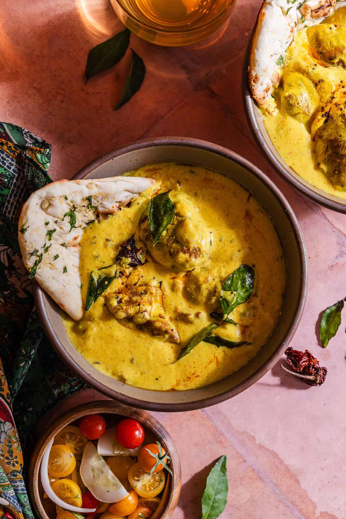Two bowls of curry with bread and vegetables.