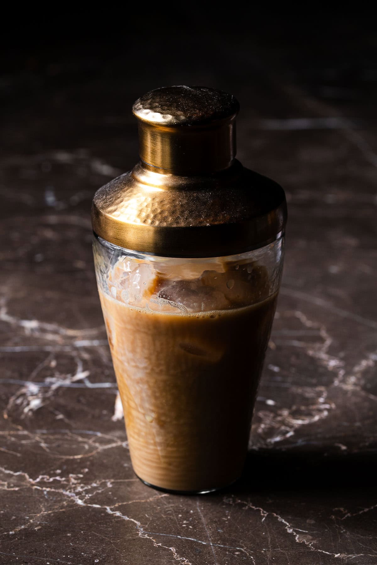Ingredients for a chai espresso martini in a cocktail shaker with ice.