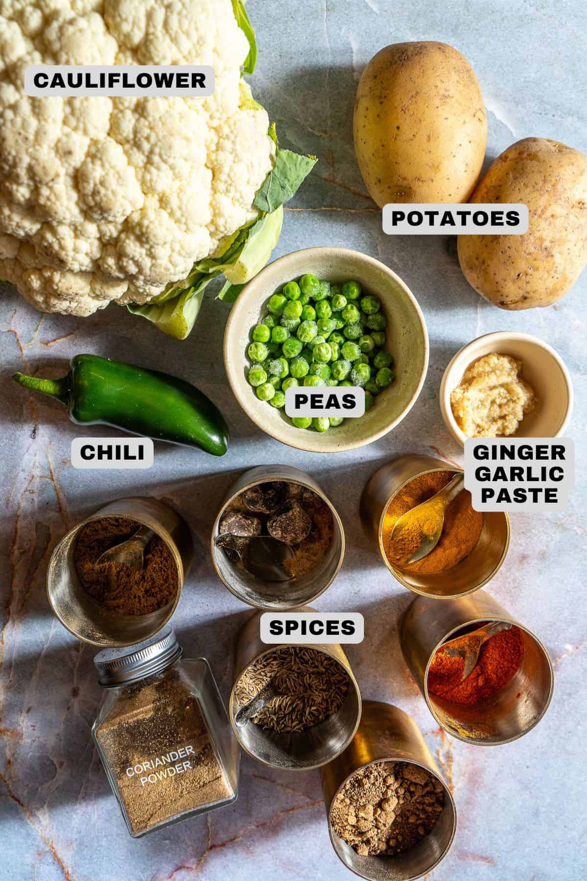 Cauliflower, potatoes, peas, chili, ginger garlic paste, spices ingredients with labels.