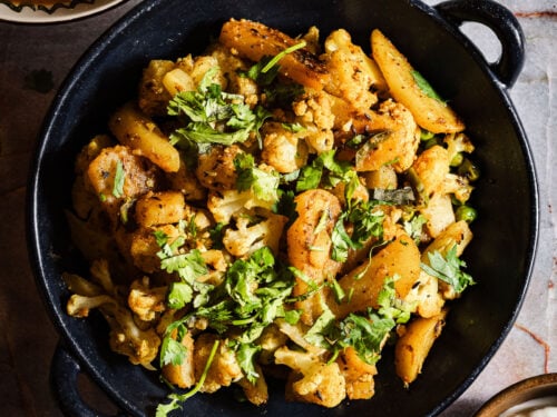 Aloo gobi with paratha, dahi, and rajma in separate bowls and plates.