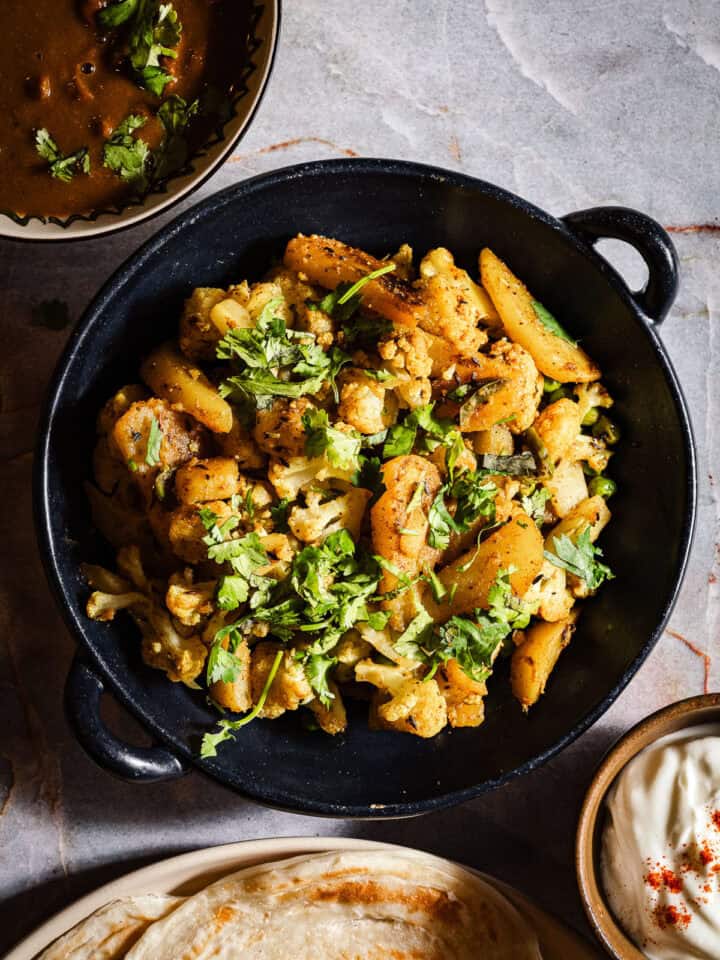 Aloo gobi with paratha, dahi, and rajma in separate bowls and plates.