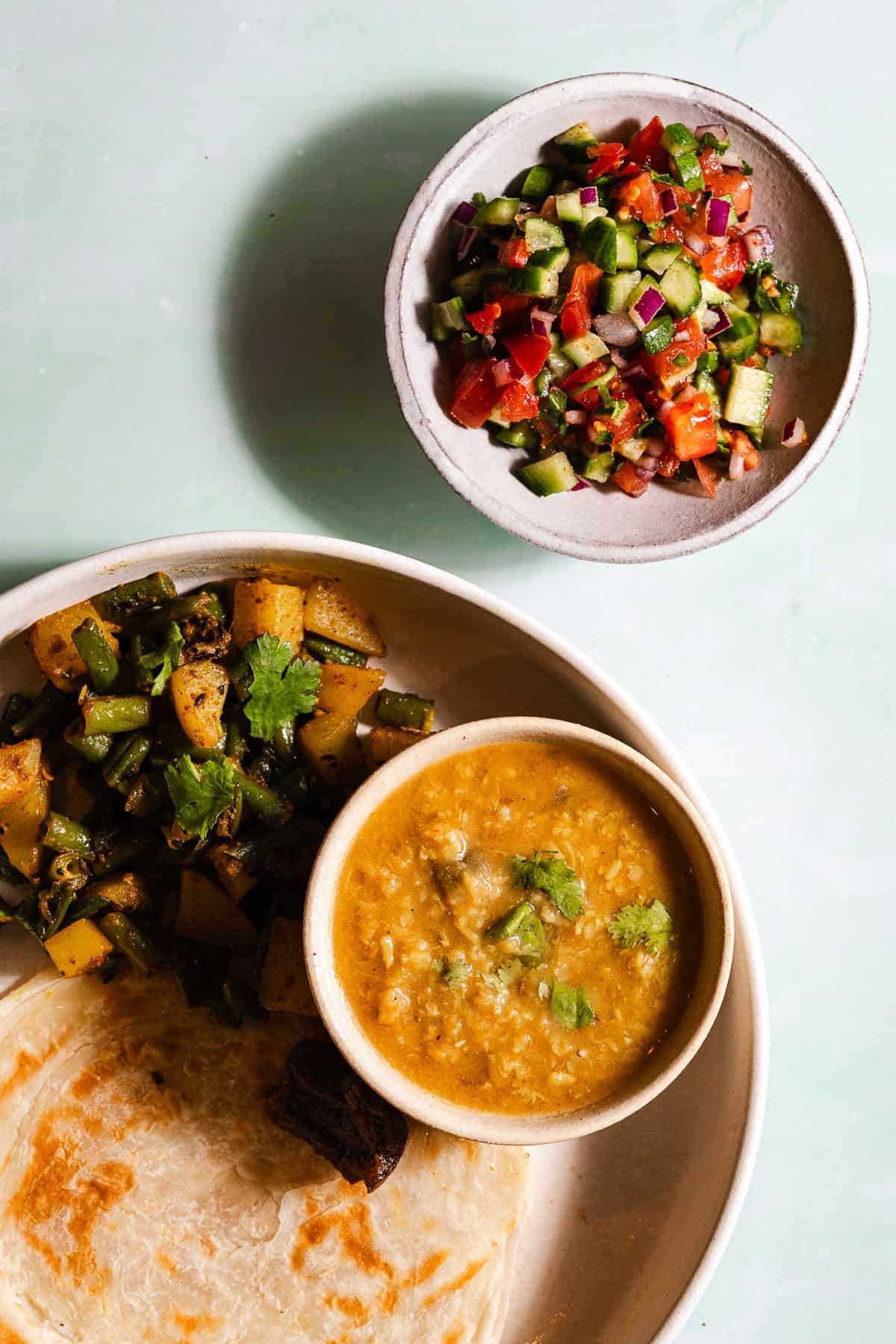 Indian kachumber salad on the side of an Indian meal of dal, paratha, and green bean aloo sabji.