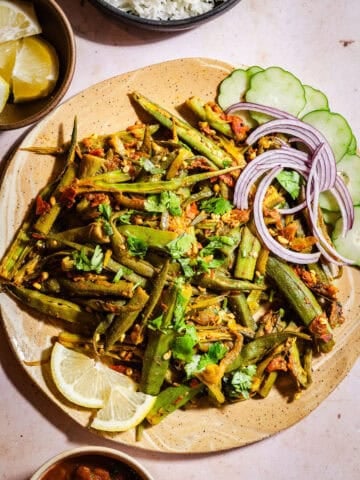 Bhindi masala in a plate with lemon slices, onions, cucumbers served with rice and rajma.