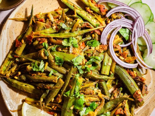 Bhindi masala in a plate with lemon slices, onions, cucumbers served with rice and rajma.