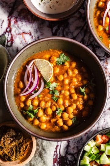 Bowls of Chole with sides of achaar, dahi, and kachumber salad.