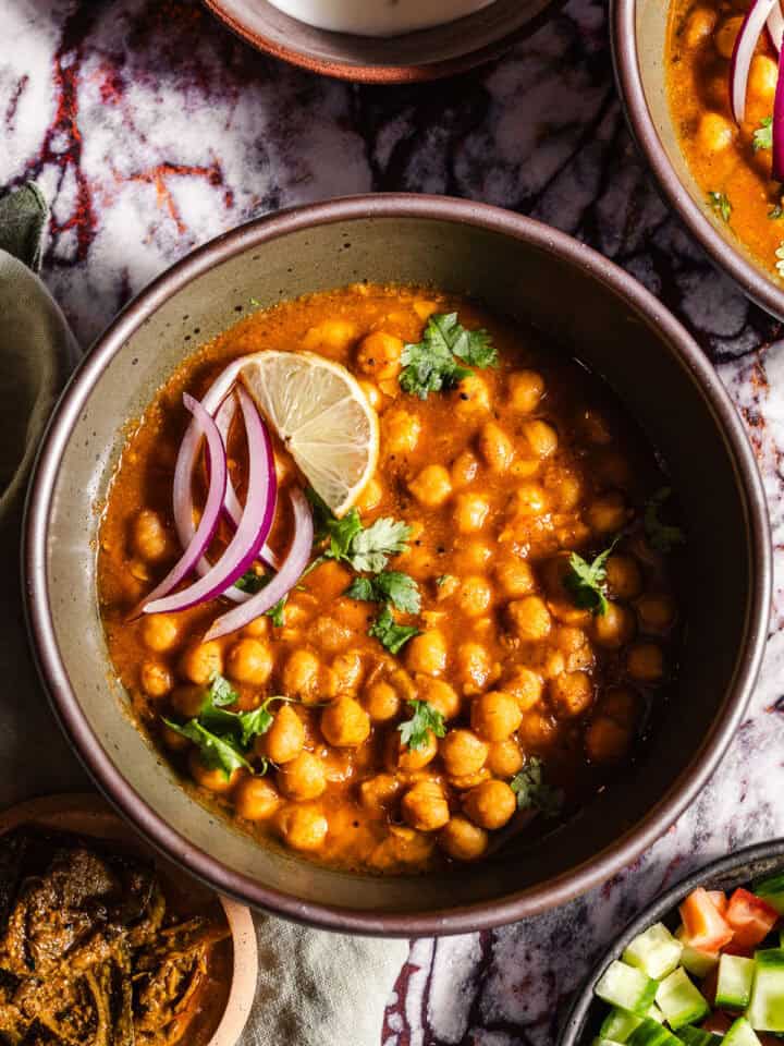 Bowls of Chole with sides of achaar, dahi, and kachumber salad.