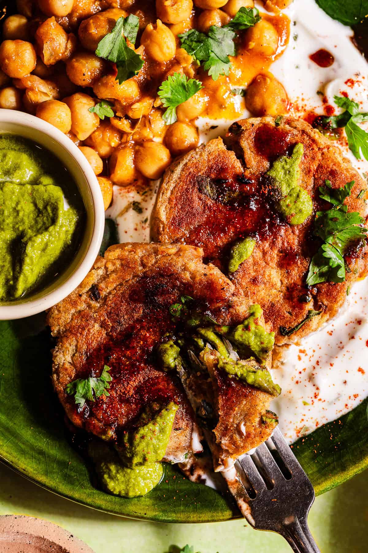 A fork digging into aloo tikkis with chutneys layers on dahi and chole.