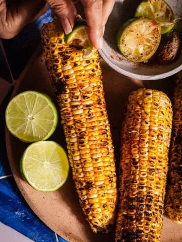 Rubbing a masala covered lime wedge on grilled corn.