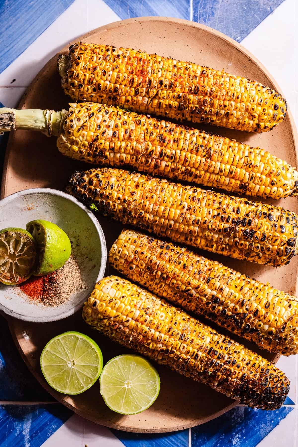 A platter filled with grilled corn on the cob with lime wedges and masala.