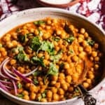 A serving bowl of chole garnished with cilantro and red onions.