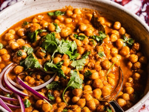 A serving bowl of chole garnished with cilantro and red onions.