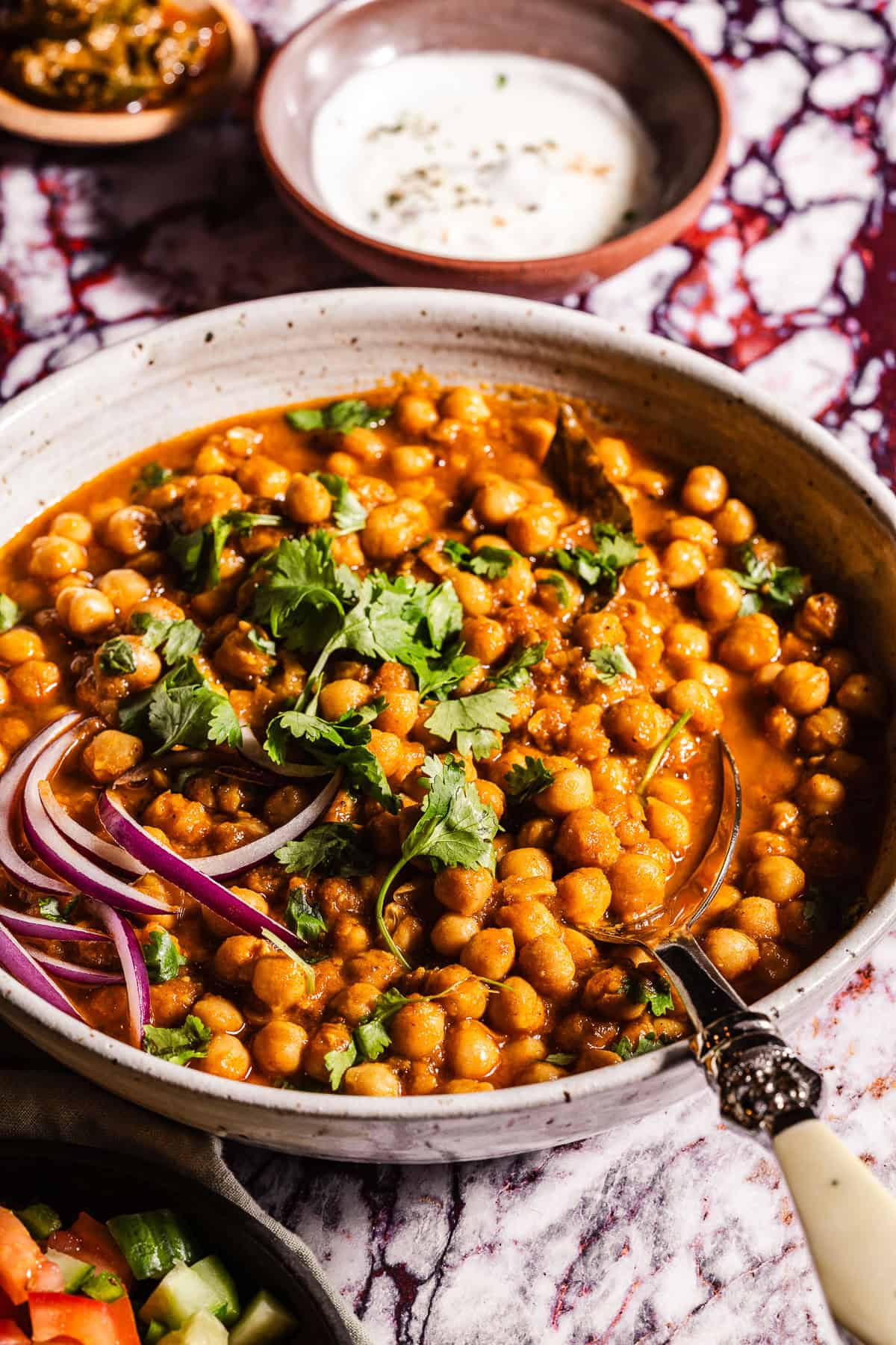A serving bowl of chole garnished with cilantro and red onions.