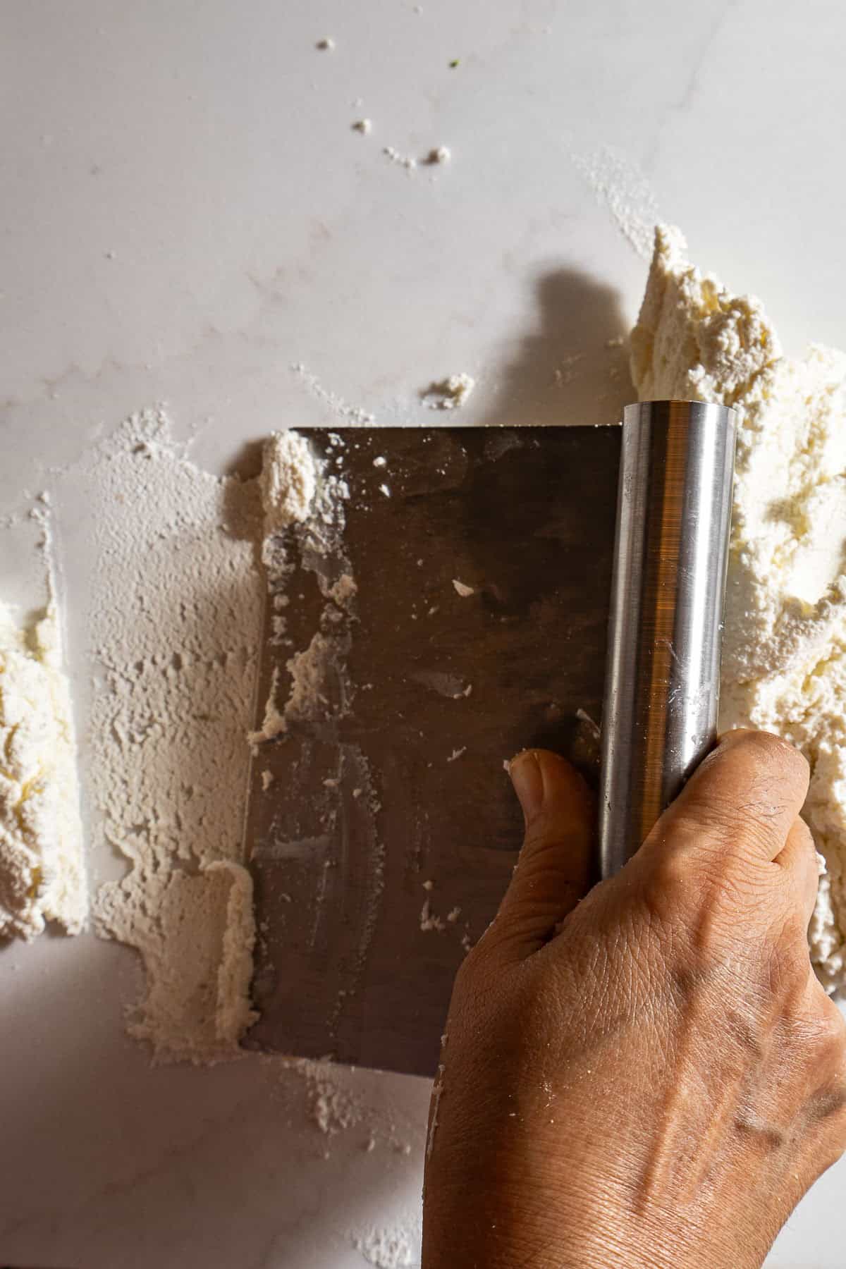 A bench scraper smoothing out the chenna.