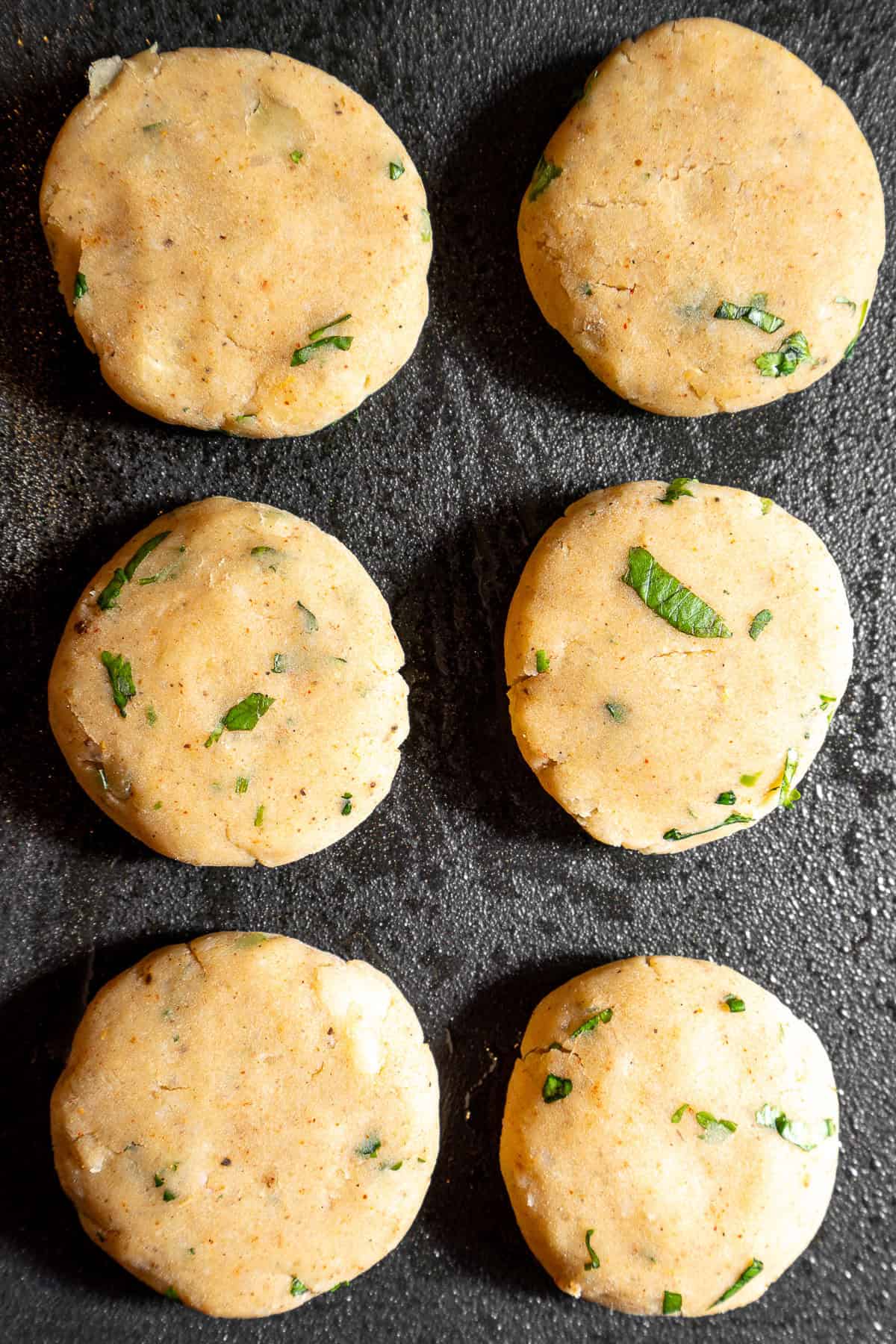 Uncooked aloo tikkis on a griddle pan.