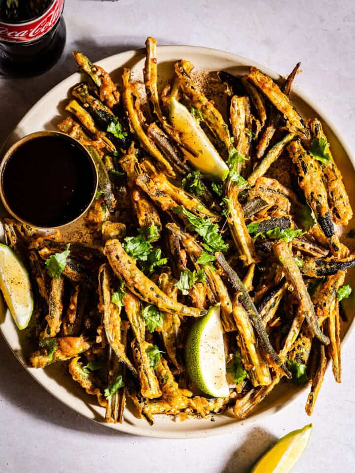 Kukuri bhindi served in a plate with chutney and lime wedges.