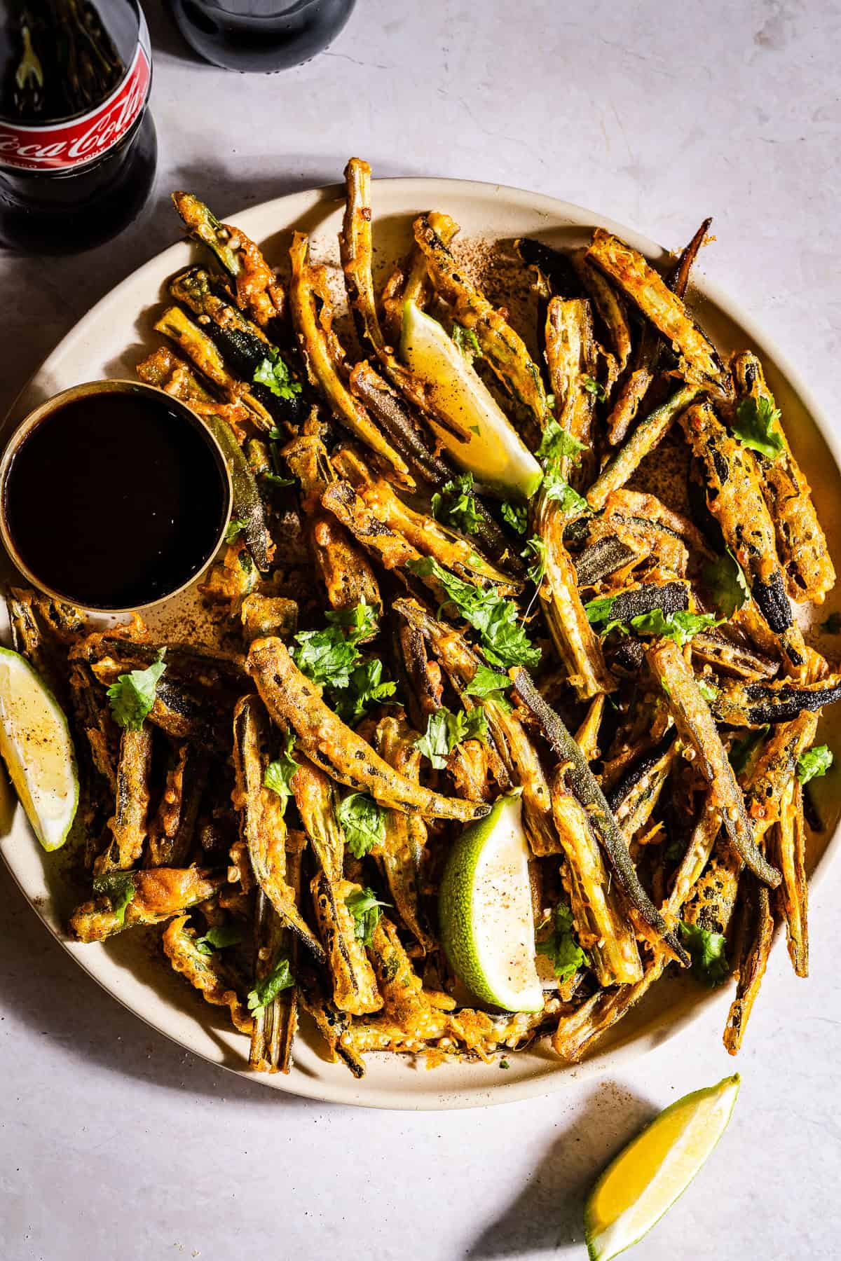 Kukuri bhindi served in a plate with chutney and lime wedges.