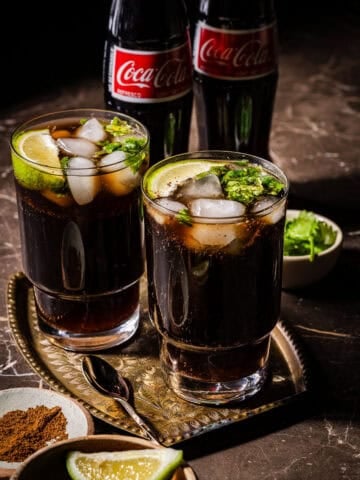 Two glasses of masala coke with coke bottles in the back.
