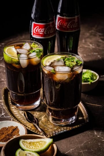 Two glasses of masala coke with coke bottles in the back.
