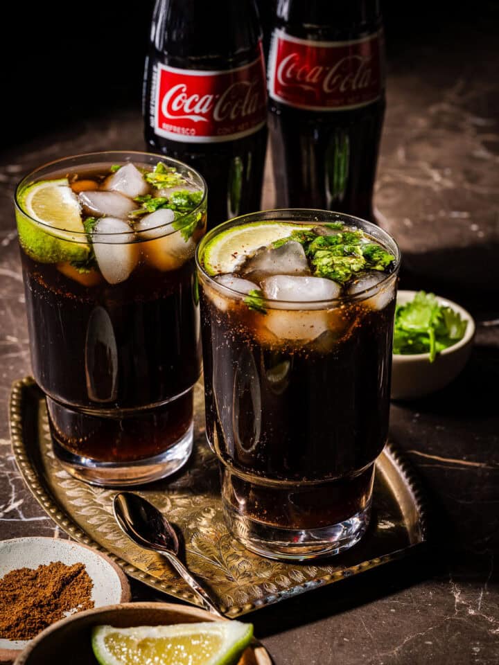 Two glasses of masala coke with coke bottles in the back.