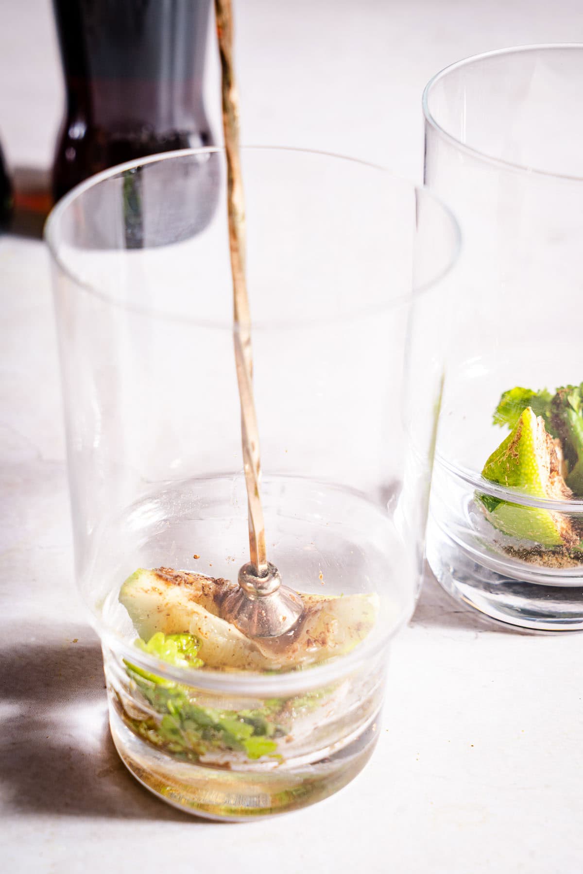 Muddling lemon with spices and cilantro in a glass.