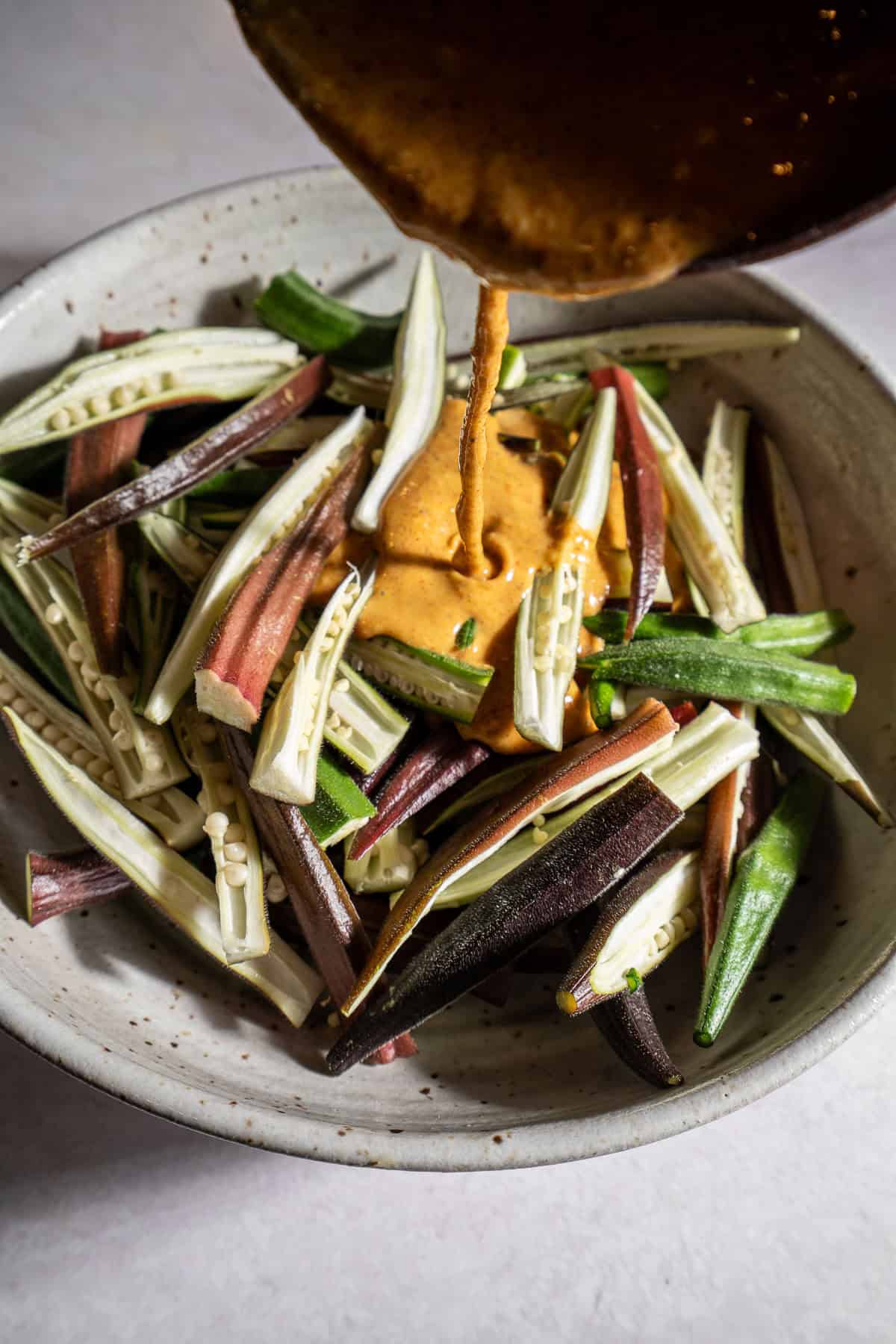 Pouring batter over halved bhindi in a bowl.