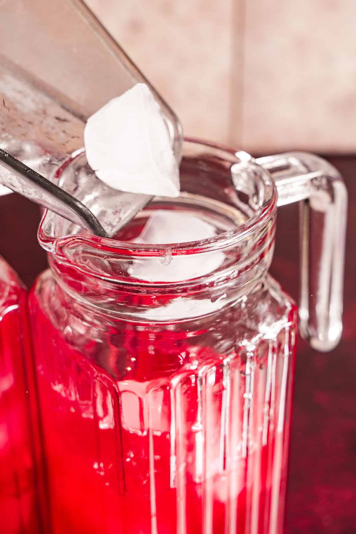 Adding ice to the pitcher of hibiscus lemonade concentrate.