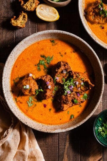 Lauki Kofta curry in bowls garnished with cilantro and diced red onions.