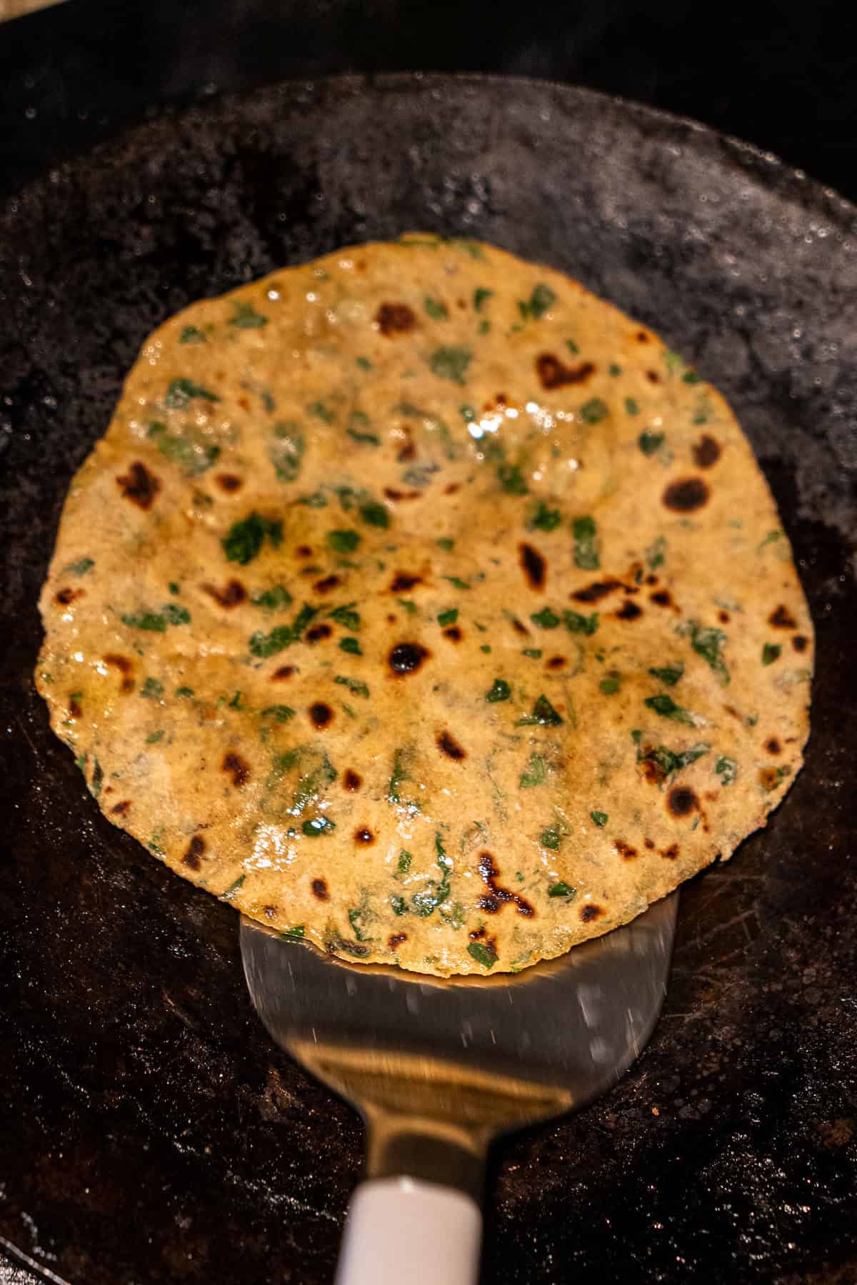 Flipping a cooked methi paratha covered in oil.