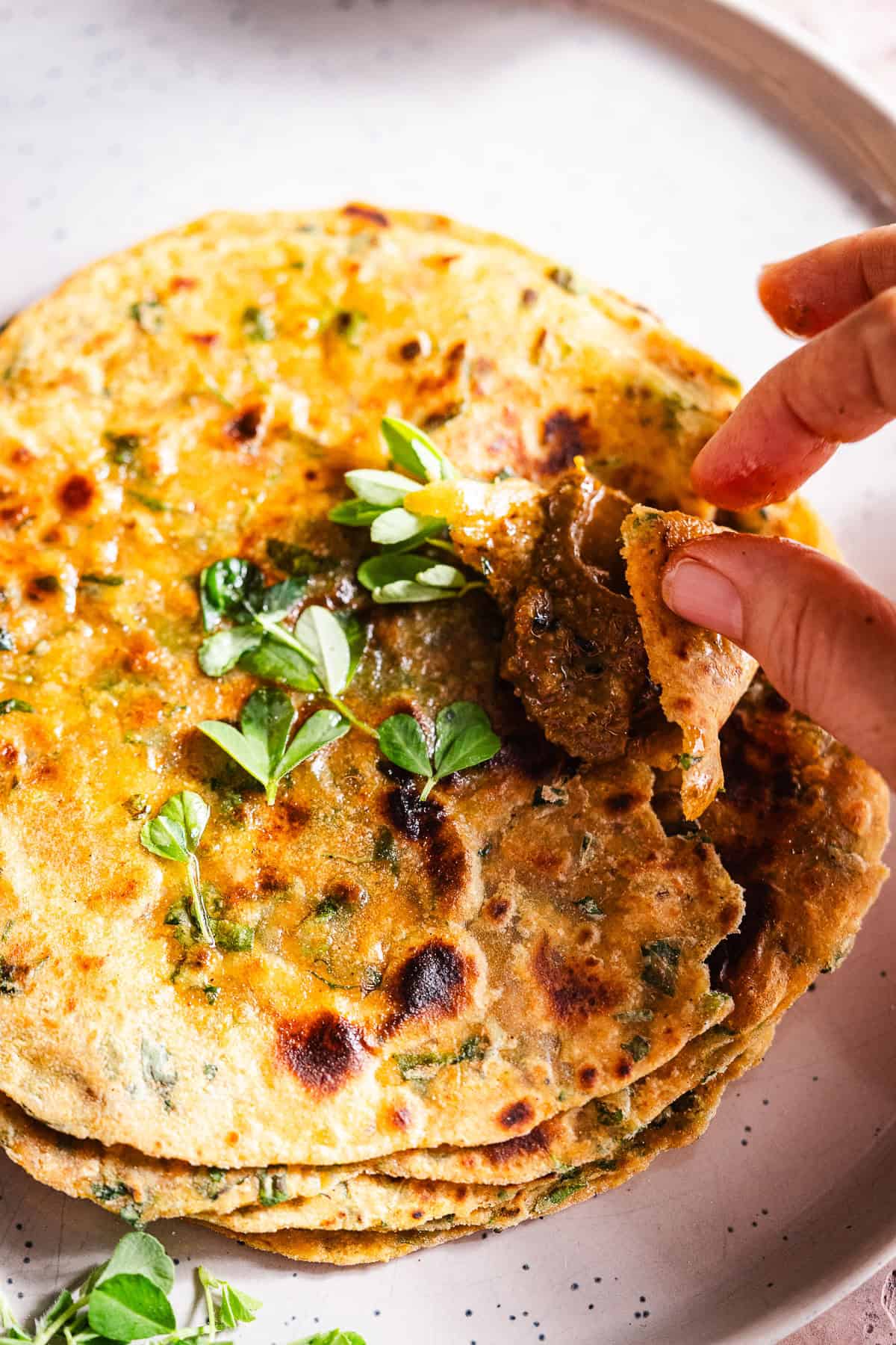 A hand picking up achaar from a paratha.
