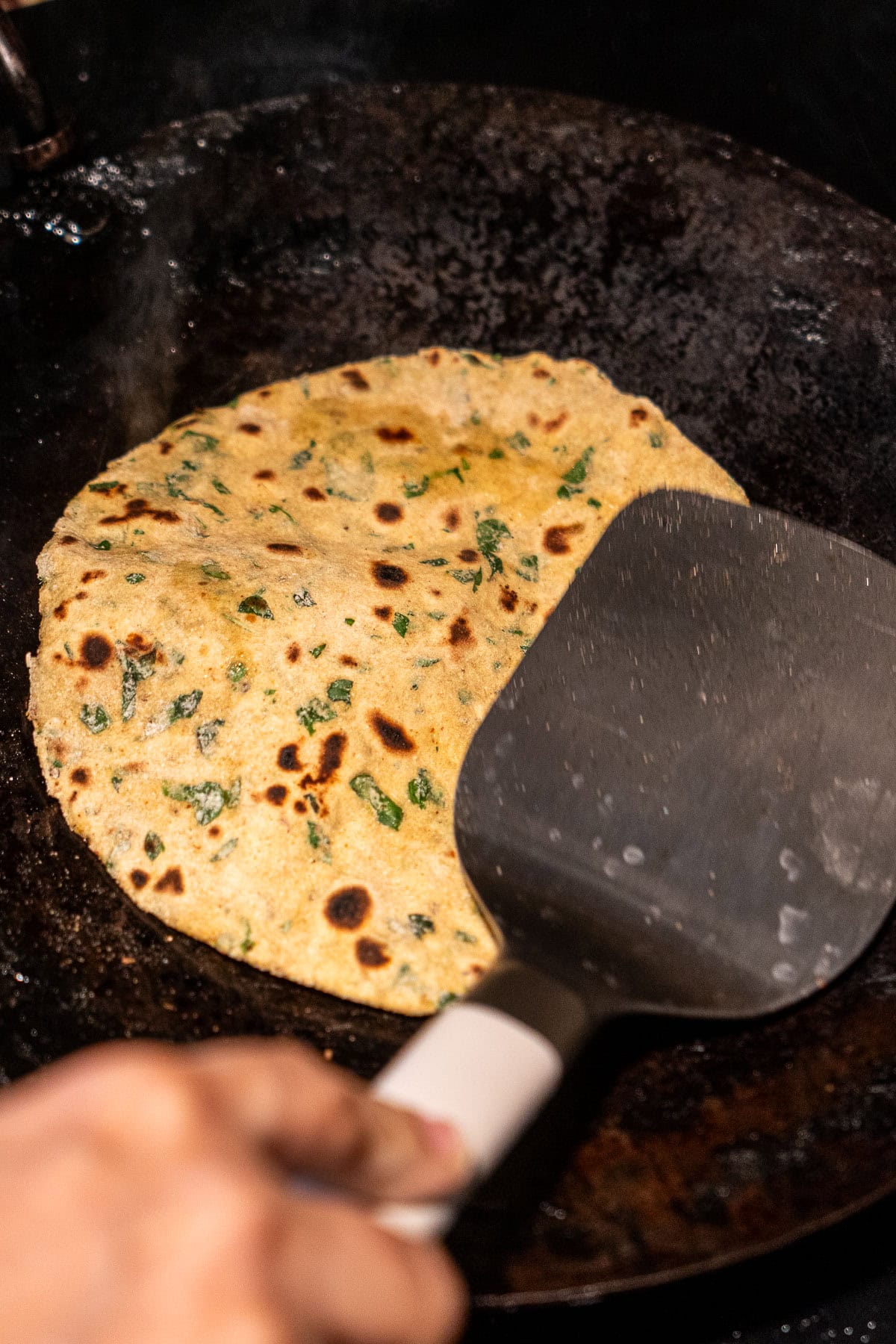 A spatula pressing a half-cooked methi paratha on a tawa.