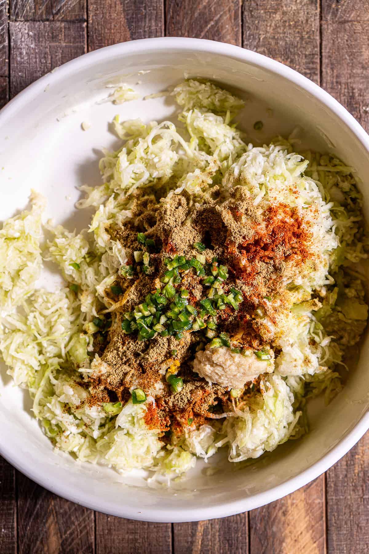A mixing bowl with shredded bottle gourd topped with spices, ginger garlic paste, and diced chilis.