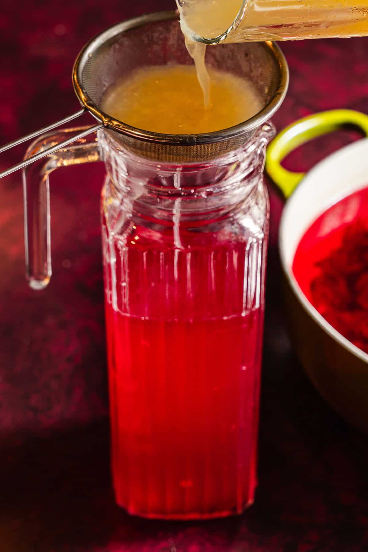 Straining lemon juice into a pitcher of hibiscus tea.