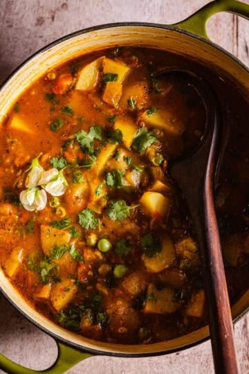 Dutch oven of aloo matar with a wooden serving spoon.