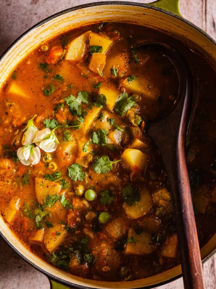 Dutch oven of aloo matar with a wooden serving spoon.