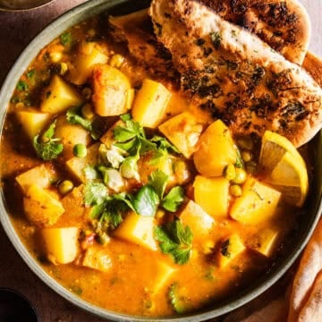 Bowl of aloo matar served with naan and dahi.