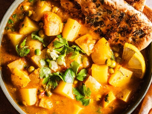 Bowl of aloo matar served with naan and dahi.