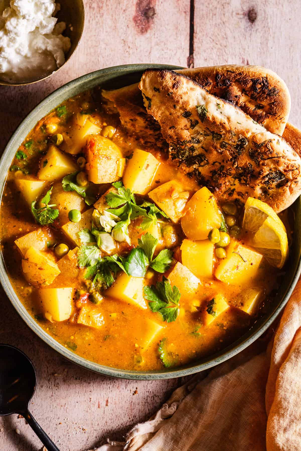 Bowl of aloo matar served with naan and dahi.