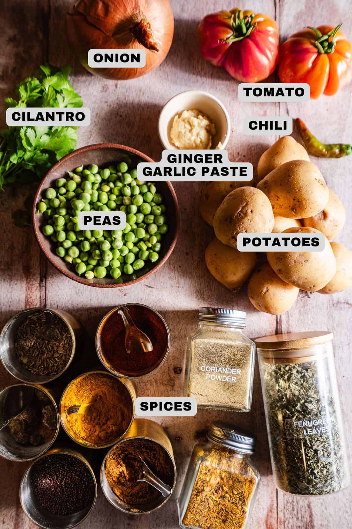Onion, tomato, chili, ginger garlic paste, cilantro, peas, potatoes, and spices ingredients with labels.