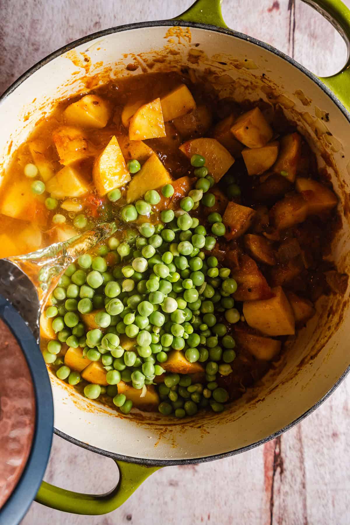 Pouring water into peas and potatoes over tomato gravy.