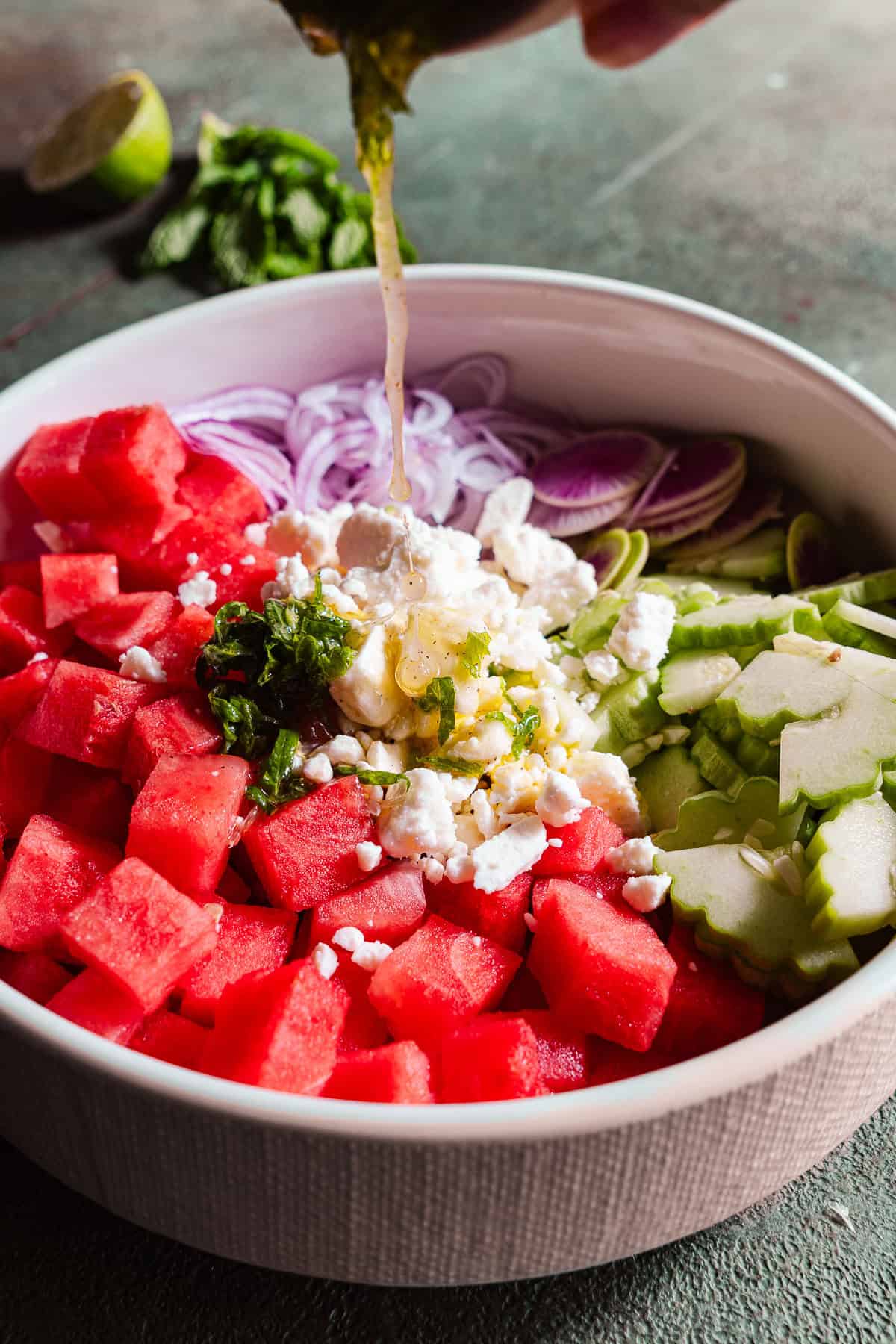 Pouring the citrus olive oil dressing on top of the unmixed watermelon feta salad.