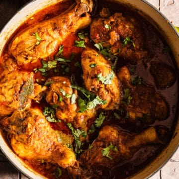 Cooked chicken curry in a dutch oven served with rice and chili peppers.