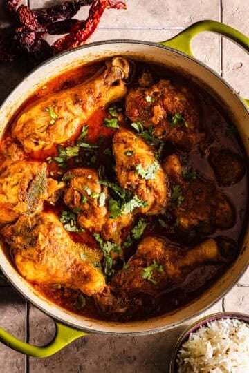 Cooked chicken curry in a dutch oven served with rice and chili peppers.