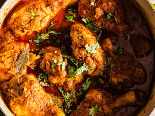 Cooked chicken curry in a dutch oven served with rice and chili peppers.
